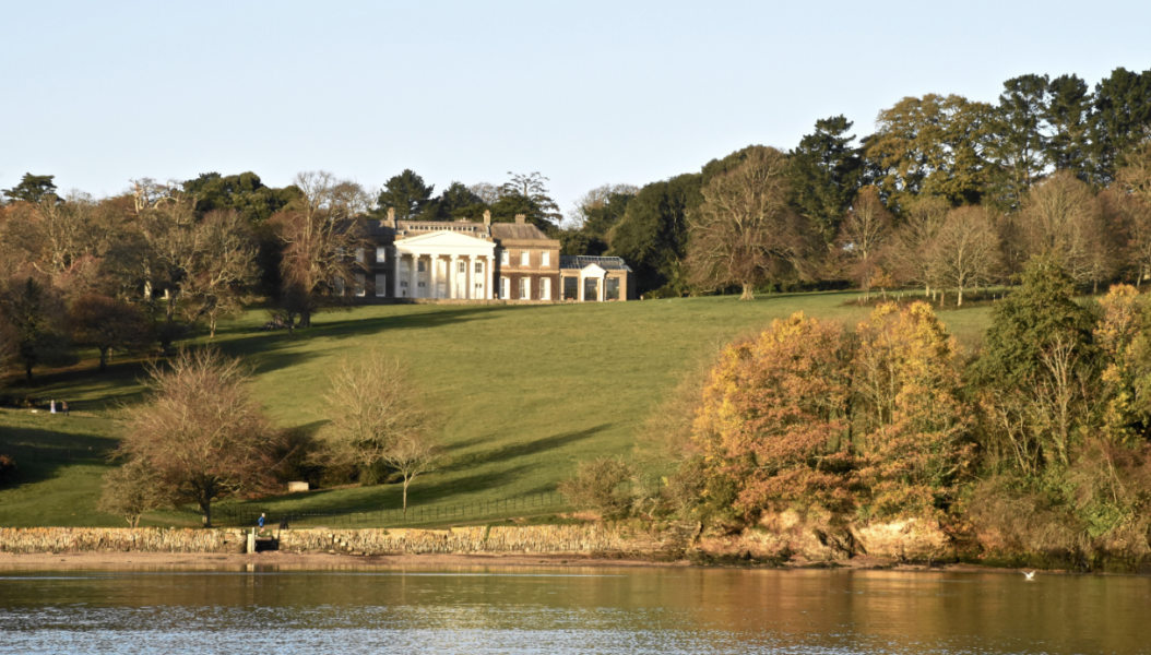 Visit Trelissick in October half term when visiting Cornwall. Photo of Trelissick estate over the water of the river Fal with autumnal setting, brown leaves in trees and large 1750s home at the top of the hill.