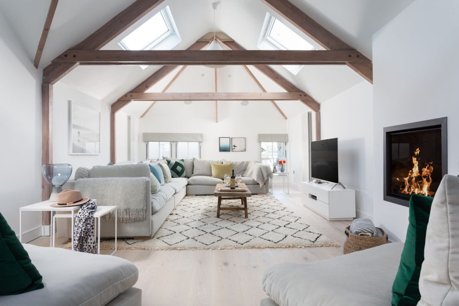 St Ives property let by Cornish Gems with large grey sofa, beams over the room, white rug and coffee table with TV on wall. Electric fire on wall.