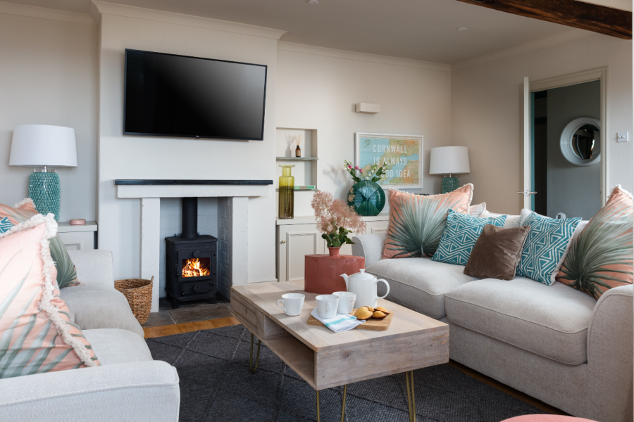 living room with log burner, coffee table, grey sofas and blue and pink cushions at dog friendly Cornwall property Chycoose let by Cornish Gems