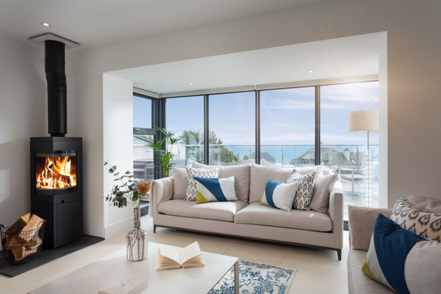 Sofa in front of wall to ceiling window with sea view coffee table with book open and fire in log burner Ilha View in Looe Cornwall let by Cornish Gems