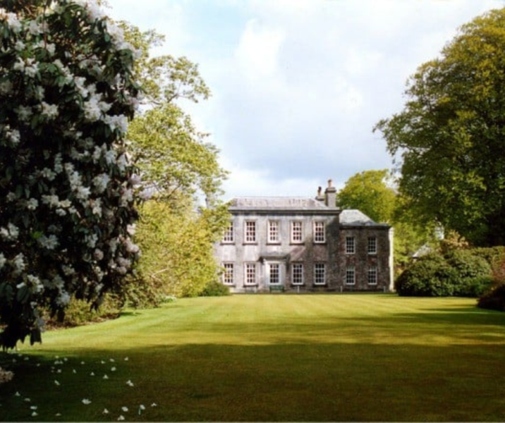 green lawn, large trees on left and right with georgian building in the background, central to photo, white clouds above